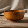 A round wooden bowl with a glossy finish, showcasing prominent vertical wood grain patterns, set against a plain white background.